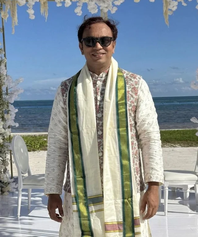 Pandit Jinit Bhatt standing beside a floral wedding arch by the ocean